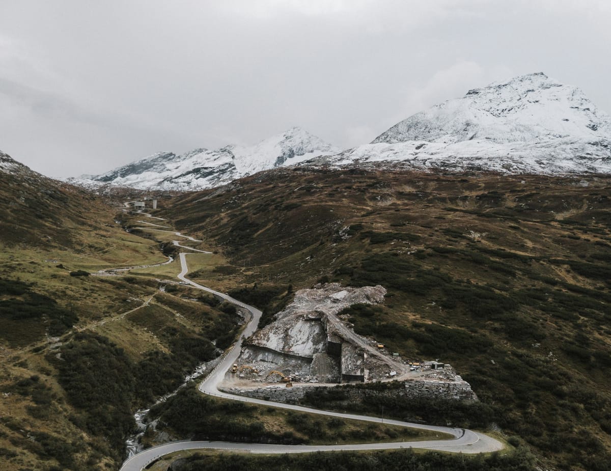 A winding road cuts through a mountainous region, with frost covered tips in the distance.