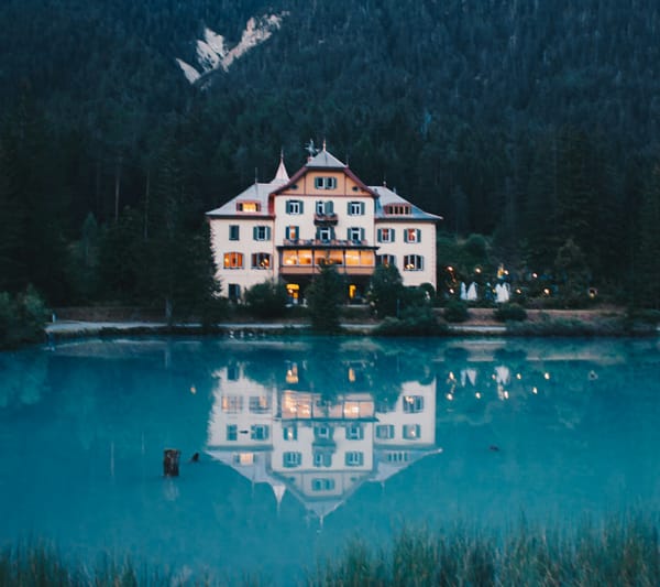 A small hotel in front of a lake and surrounded by trees.