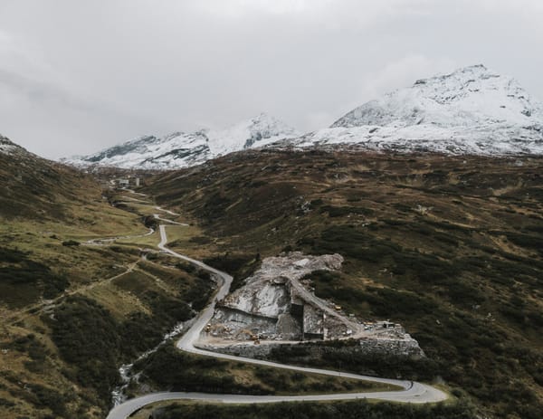 A winding road cuts through a mountainous region, with frost covered tips in the distance.