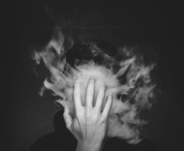 Black and white photo of a person holding a hand to their face, which is obscurred by heavy smoke.