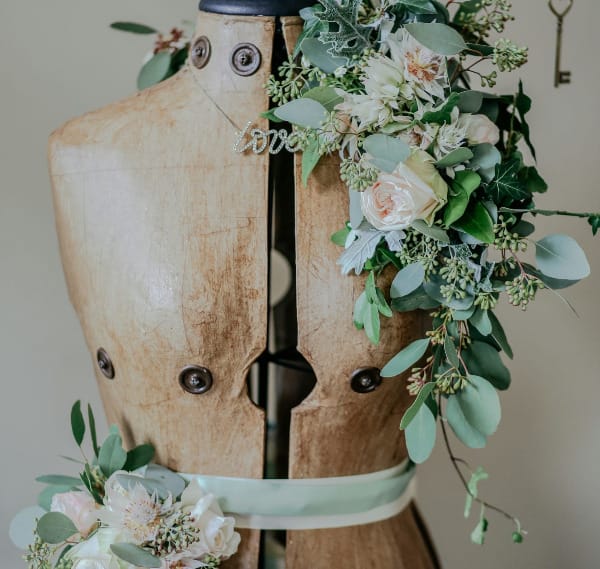 A brown mannequin, sporting garlands of fake roses and greenery.
