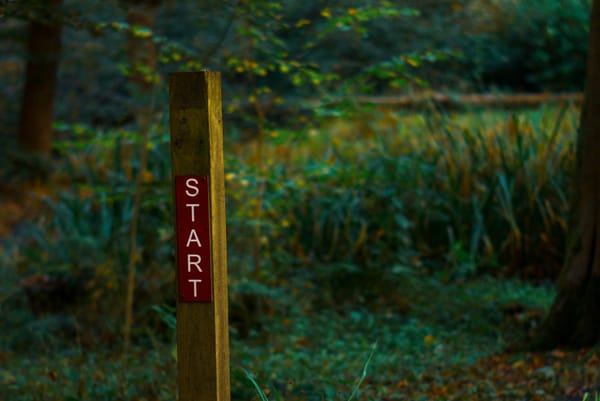 A sign post on a path surrounded by greenery. The post simply says "Start".