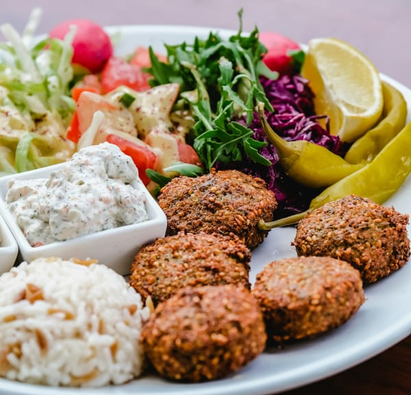A plate of falafels, assorted veggies, a small pat of rice, and dip.